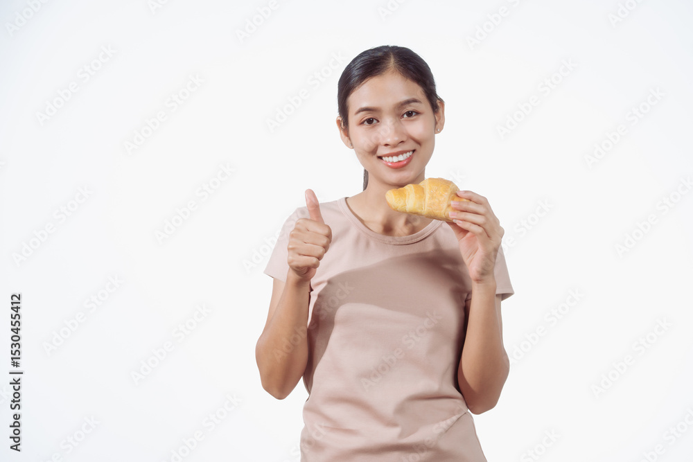 A confident young Asian woman in a light brown shirt stands against a white background, happily holding a delicious croissant in her hand, ready to enjoy a fresh and tasty pastry snack. A confident young Asian woman in a light brown shirt stands against a white background, happily holding a delicious croissant in her hand, ready to enjoy a fresh and tasty pastry snack.