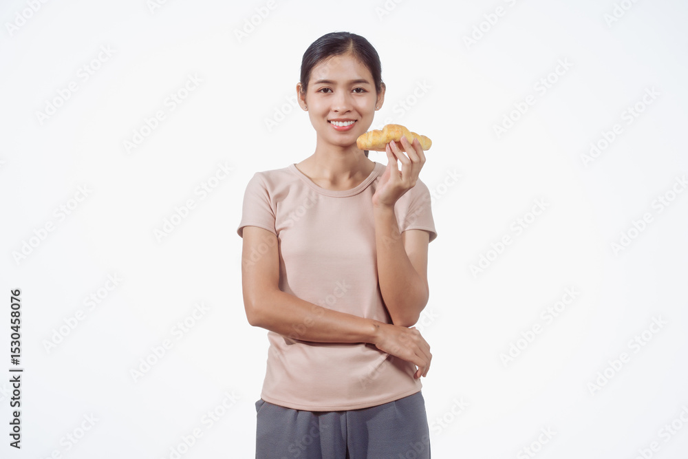 A confident young Asian woman in a light brown shirt stands against a white background, happily holding a delicious croissant in her hand, ready to enjoy a fresh and tasty pastry snack. A confident young Asian woman in a light brown shirt stands against a white background, happily holding a delicious croissant in her hand, ready to enjoy a fresh and tasty pastry snack.