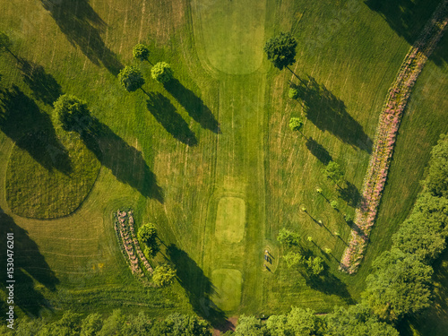 Drone image of a golf course tee area and fairway with long tree shadows and landscaped surroundings in evening light. Ideal for sport, nature, and outdoor themes.