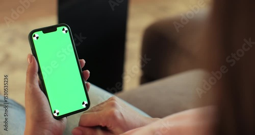 Female using smartphone with green screen mock up display at home. Browsing the internet and checking videos on social networks.