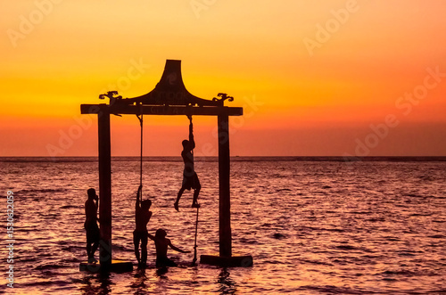 Friends playing on a swing at sunset in gili trawangan, indonesia