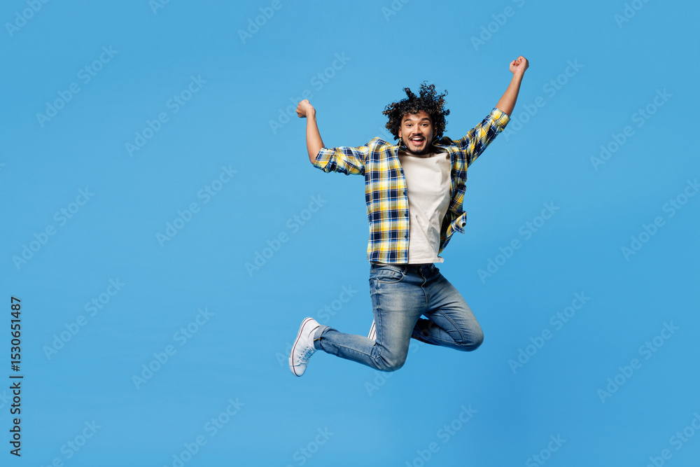 Full body young cool happy Indian man he wear yellow checkered shirt casual clothes jump high do winner gesture clench fists isolated on plain blue cyan background studio portrait. Lifestyle concept. Full body young cool happy Indian man he wear yellow checkered shirt casual clothes jump high do winner gesture clench fists isolated on plain blue cyan background studio portrait. Lifestyle concept.