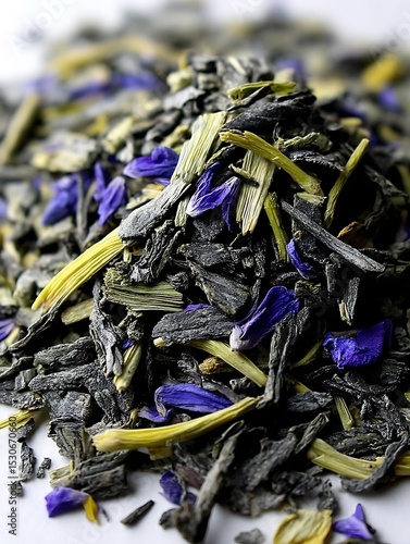 the image shows a close up of a pile of loose tea blend on a white surface. the tea consists of dark, curled leaves mixed with pale yellow stems and vibrant blue flower petals