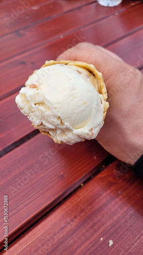 Glace en cornet dans main auprès d'une table en bois rouge