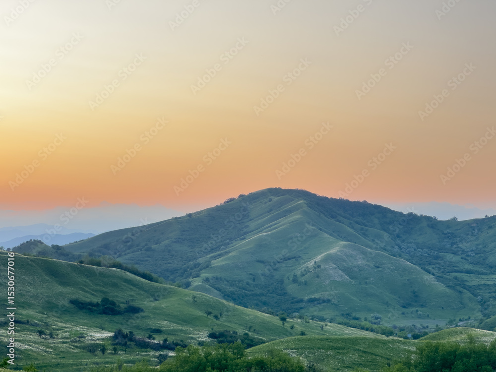 Obraz premium Buzău Green Hills Sunset. A serene landscape view captures rolling green hills in Buzău County, Romania, bathed in the warm hues of a sunset. 