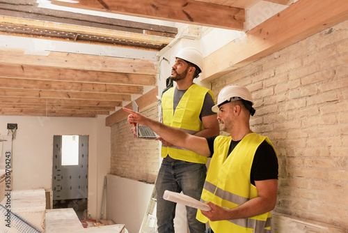 Photography Two male Construction workers with laptop inspecting ceiling structure at renova