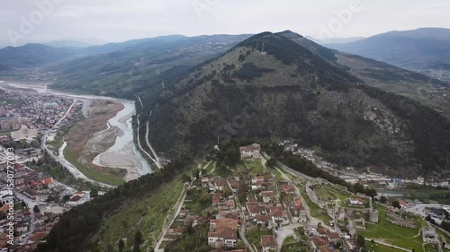 Forward drone shot over the ancient castle of Berat in Albania, gradually revealing the traditional old town below, framed by lush mountains and the winding Osum River.