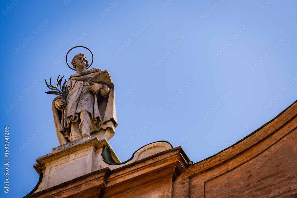 Obraz premium Marble statue of saint above church entrance, shot against clear blue sky in Italy 