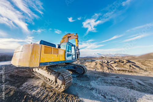 Yellow crawler excavator with hydraulic breaker on construction site under clear blue sky