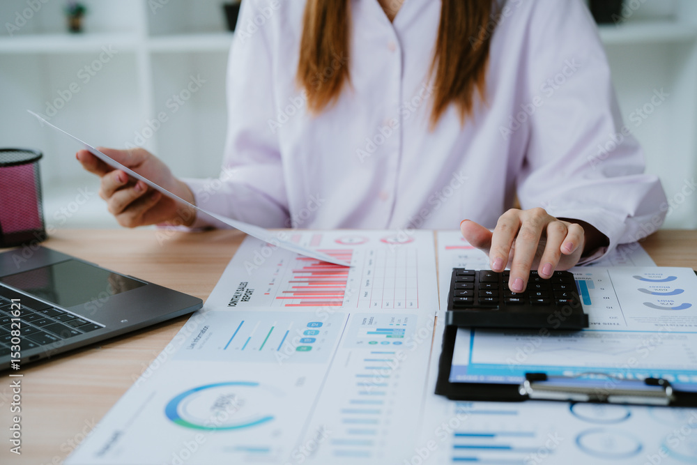 Fototapeta premium Businesswoman analyzing financial charts and using calculator in office