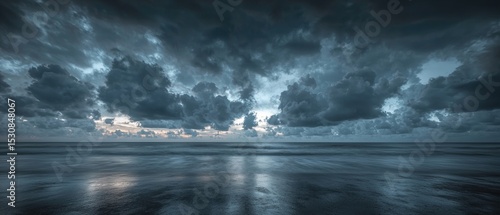 Dark, brooding clouds dominate a moody seascape, their reflections mirrored in the still, dark waters of the beach at sunset or sunrise