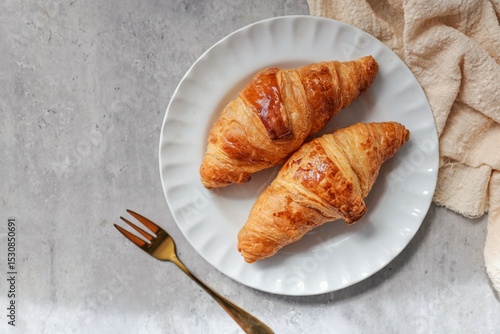 Two croissant in white plate on grey background , top view food table