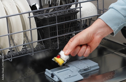 Emptying the dishwasher and placing a detergent pod in the compartment in a modern kitchen 