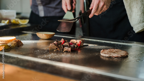 Fotografija Grilling meat skewers and burger patty on a teppanyaki grill