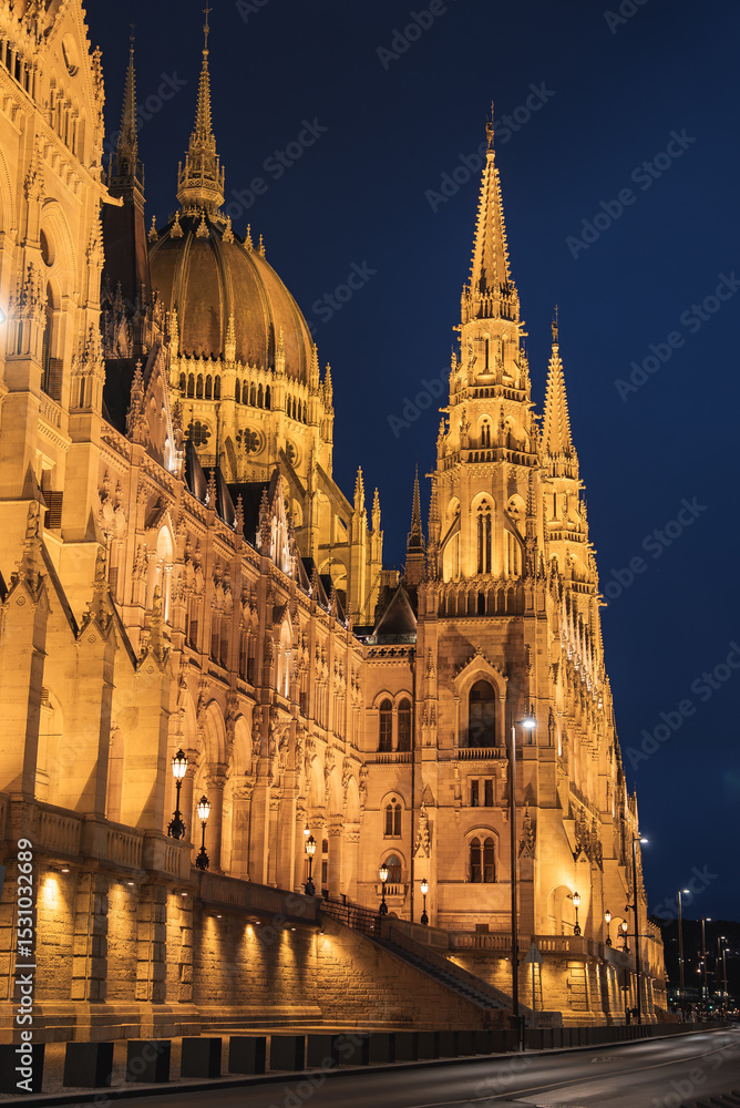 Obraz premium The Hungarian Parliament Building in Budapest, Hungary, glows warmly at night, showcasing its neo Gothic spires, domes, and intricate stonework.