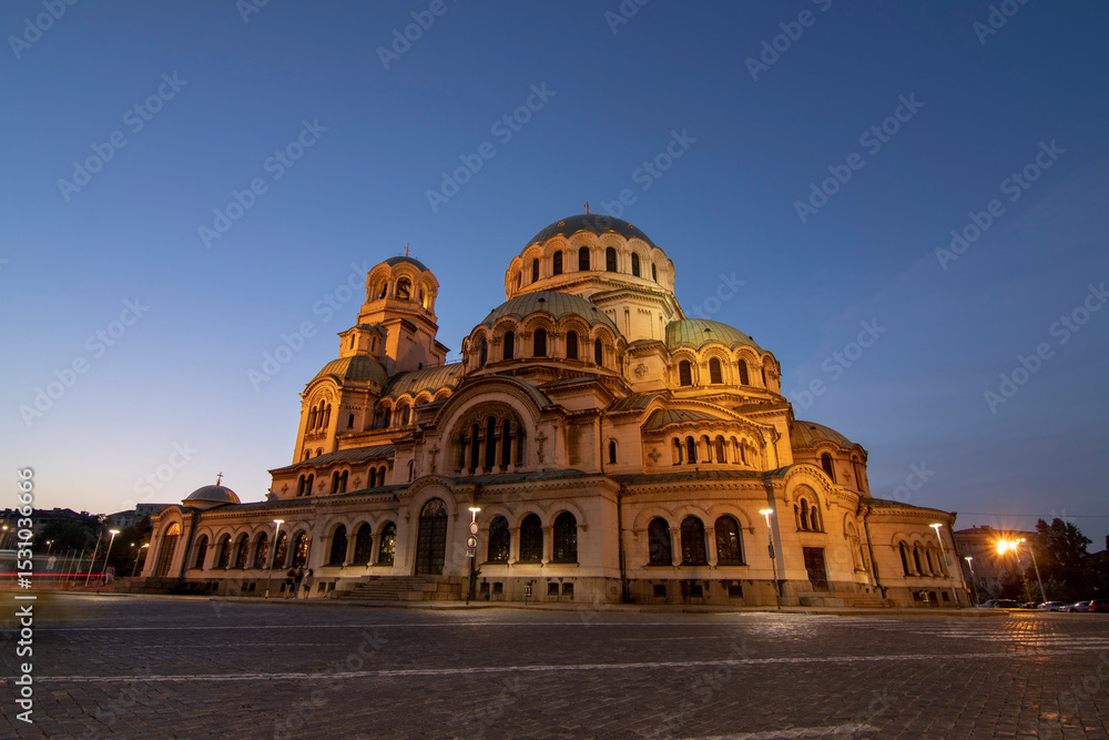 Obraz premium Alexander Nevsky Cathedral in Sofia at dusk, bathed in warm light, showcasing its grand Neo-Byzantine architecture and intricate domes under a fading blue sky.