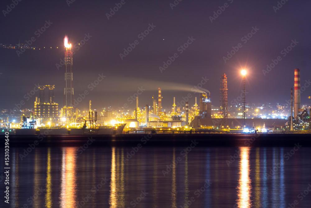 Fototapeta premium Brightly lit İzmit Tüpraş oil refinery at night, reflecting on calm waters. Perfect for energy, industrial, environmental, and commercial projects needing striking, high-resolution imagery.
