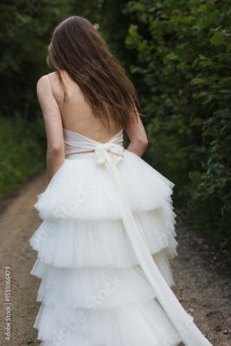 Bride in a modern, layered white tulle dress walking down a country path, captured from behind in natural light.