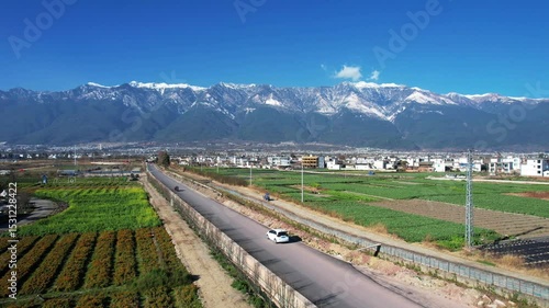 Cars driving on road with Cangshan Mountain background in Dali Yunnan Province, China. Aerial view of rural traffic