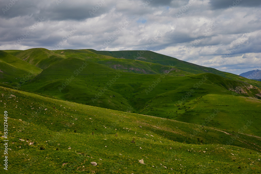 Scenic view of lush green hills and dramatic red cliffs under a bright blue sky with white clouds, showcasing the beauty of untouched mountainous nature and diverse rocky terrain. Scenic view of lush green hills and dramatic red cliffs under a bright blue sky with white clouds, showcasing the beauty of untouched mountainous nature and diverse rocky terrain.