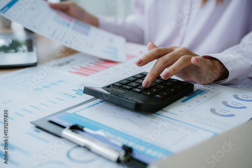 Businesswoman analyzing financial charts and using calculator in office