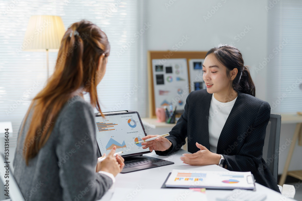 Businesswomen using a tablet and printed documents are discussing and analyzing financial charts, working together in the office Businesswomen using a tablet and printed documents are discussing and analyzing financial charts, working together in the office