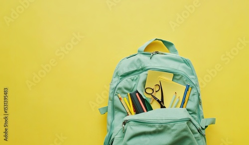 Teal backpack filled with school supplies on a bright yellow background