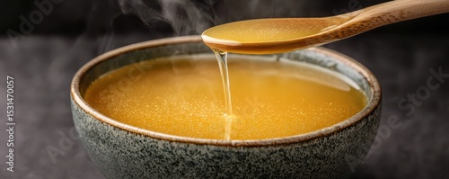 Hot golden broth steaming in a rustic bowl, with a wooden spoon drizzling the warm liquid.