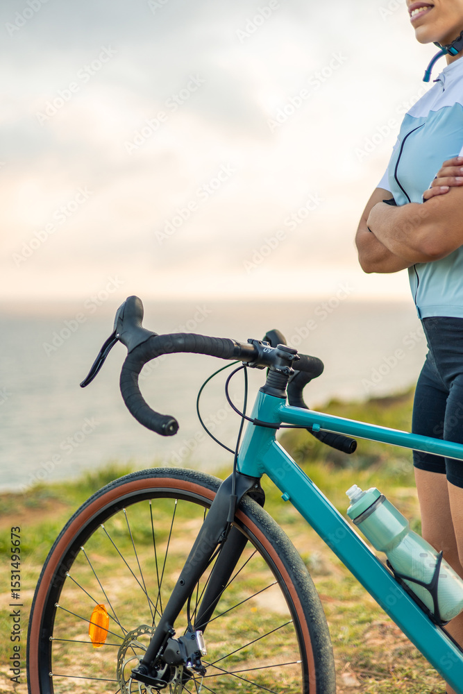 Obraz premium vertical Latin cyclist woman posing with gravel bike at sunrise by the sea
