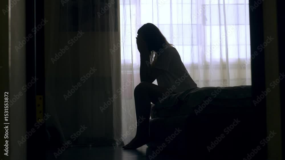 Silhouette of woman sitting on bed in the dark bedroom, depression, pain. Portrait of Unhappy sad woman sitting against window and thinking about her life Silhouette of woman sitting on bed in the dark bedroom, depression, pain. Portrait of Unhappy sad woman sitting against window and thinking about her life