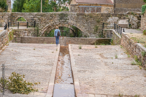 Woman walking through the old town of a village with a stream and a stone bridge in the background