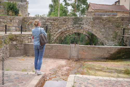 Woman walking through the old town of a village with a stream and a stone bridge in the background