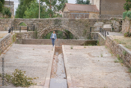 Woman walking through the old town of a village with a stream and a stone bridge in the background