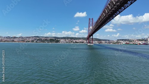 Urban drone flight under the iconic 25 de Abril Bridge in Lisbon, Portugal. Aerial scene capturing the structure’s scale, water reflections, and vibrant city energy from a dynamic, low-angle view.
