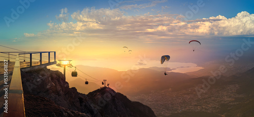 Leisure and skydiving from the Babadag mountain over the Fethiye resort, Turkey. Panoramic landscape with silhouettes of parasailing touristers flying near the top station of Oludeniz cable car.