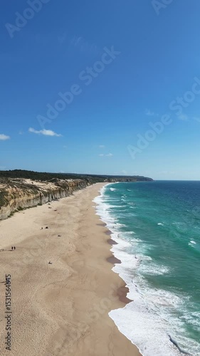 High drone view of Caparica beach near Lisbon, Portugal. Vehicle tracks drawn in the sand meet soft Atlantic waves. Aerial shot showing natural patterns and contrast between land and sea.

