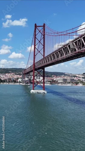 Urban drone flight under the iconic 25 de Abril Bridge in Lisbon, Portugal. Aerial scene capturing the structure’s scale, water reflections, and vibrant city energy from a dynamic, low-angle view.

