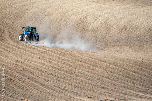 A tractor moves across freshly plowed wavy soil, highlighting agricultural machinery and rural productivity in a minimalist landscape