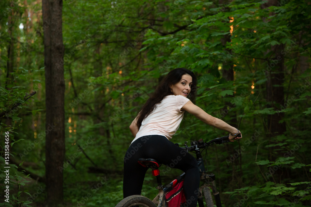 Beauty smiling sport woman biking on bicycle on path among green trees in a forest summer background. Enjoying girl outdoors. Female riding in park in sporty clothes. Back view portrait Beauty smiling sport woman biking on bicycle on path among green trees in a forest summer background. Enjoying girl outdoors. Female riding in park in sporty clothes. Back view portrait
