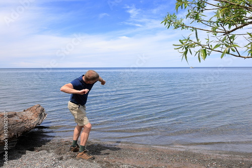 Middle-aged man in a blue shirt skips stones into a smooth blue lake