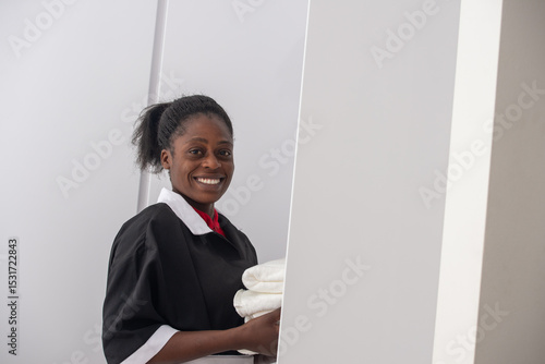 Portrait of an African woman housekeeper in uniform holding neatly folded towels.