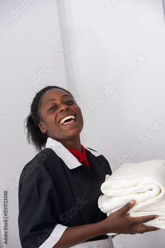 Portrait of an African woman housekeeper in uniform holding neatly folded towels.