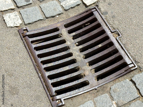 Rusty metal storm drain on cobblestone street