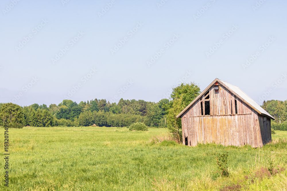 Obraz premium Old wooden barn on a grass meadow in the summer