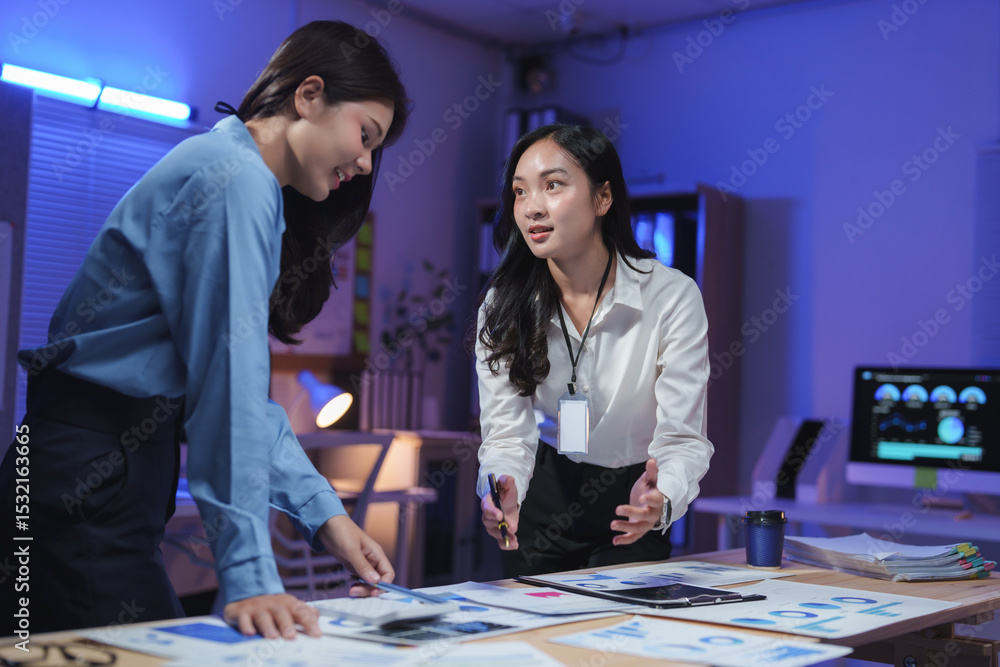Fototapeta premium Businesswomen working late analyzing financial charts in office meeting room