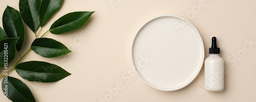 Minimalist flat lay with green leaves, an empty white round plate, and a small dropper bottle on a beige textured surface.