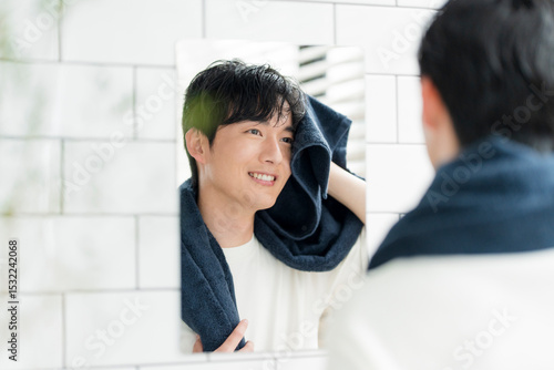 洗面所でタオルで濡れた髪を拭いている若い日本人男性