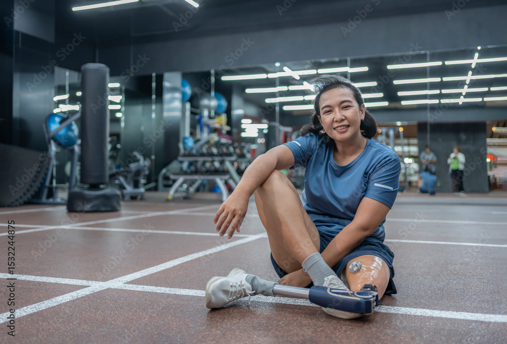 Obraz premium portrait of active asian female with prosthetic leg sitting on floor,resting during exercise in gym fitness club