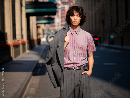 Portrait of handsome Chinese young man wearing stripe shirt posing in the street, young guy with black curly hair with urban background. Male fashion, cool Asian young man lifestyle.