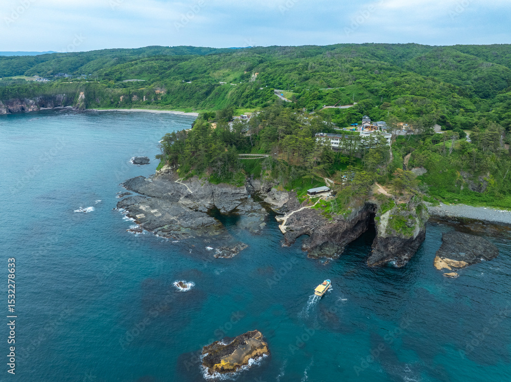 Obraz premium 石川県能登半島の名所・巌門にある自然の海蝕洞に、遊覧船が進入する様子をドローンで撮影。断崖と日本海の荒波が生んだ壮大な地形を捉えた空撮写真。